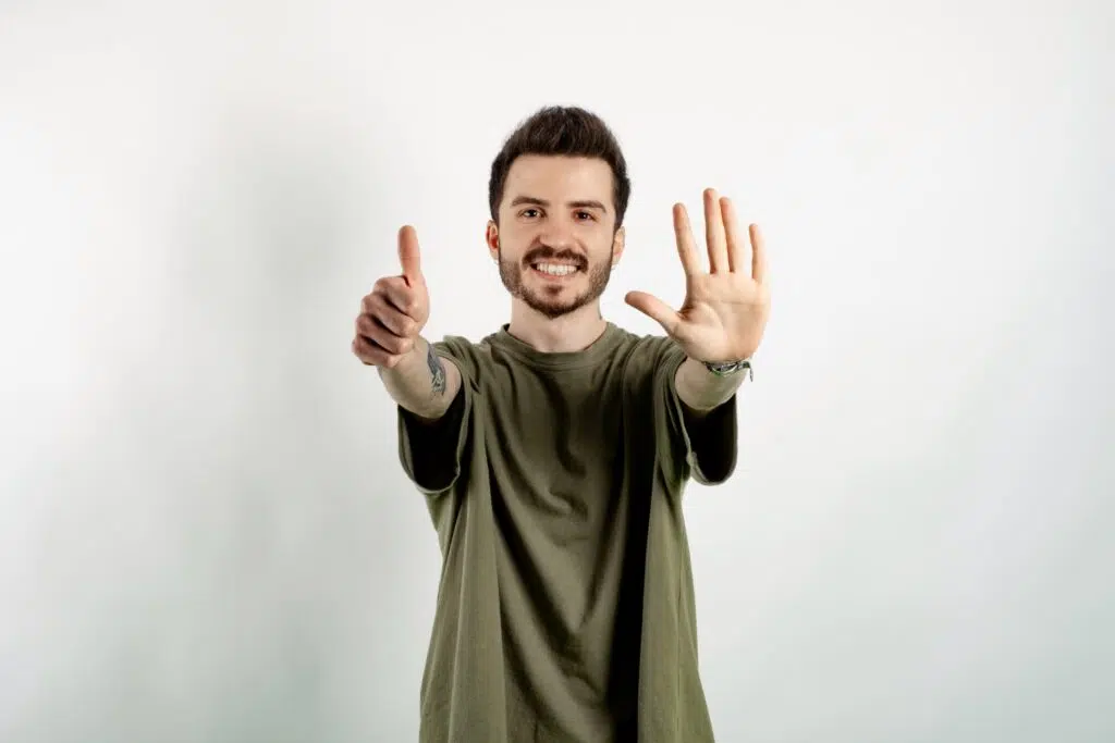 Une jeune homme souriant montrant avec ses doigts le nombre 6.