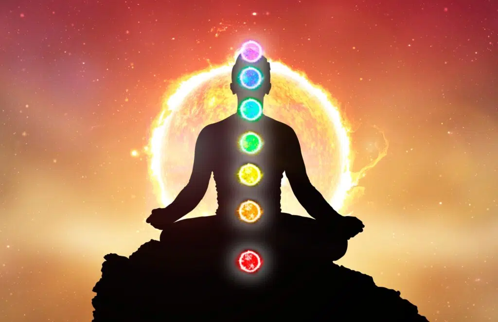 Silhouette d'un homme en position de méditation avec les différents types de chakras sur un fond de soleil.