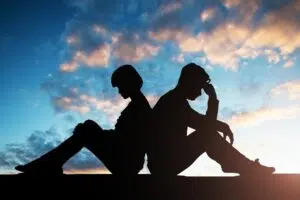 Silhouette d'un couple composé d'un homme et d'une femme, assis dos à dos et semblant tous les deux pensif. Ciel nuageux en arrière plan