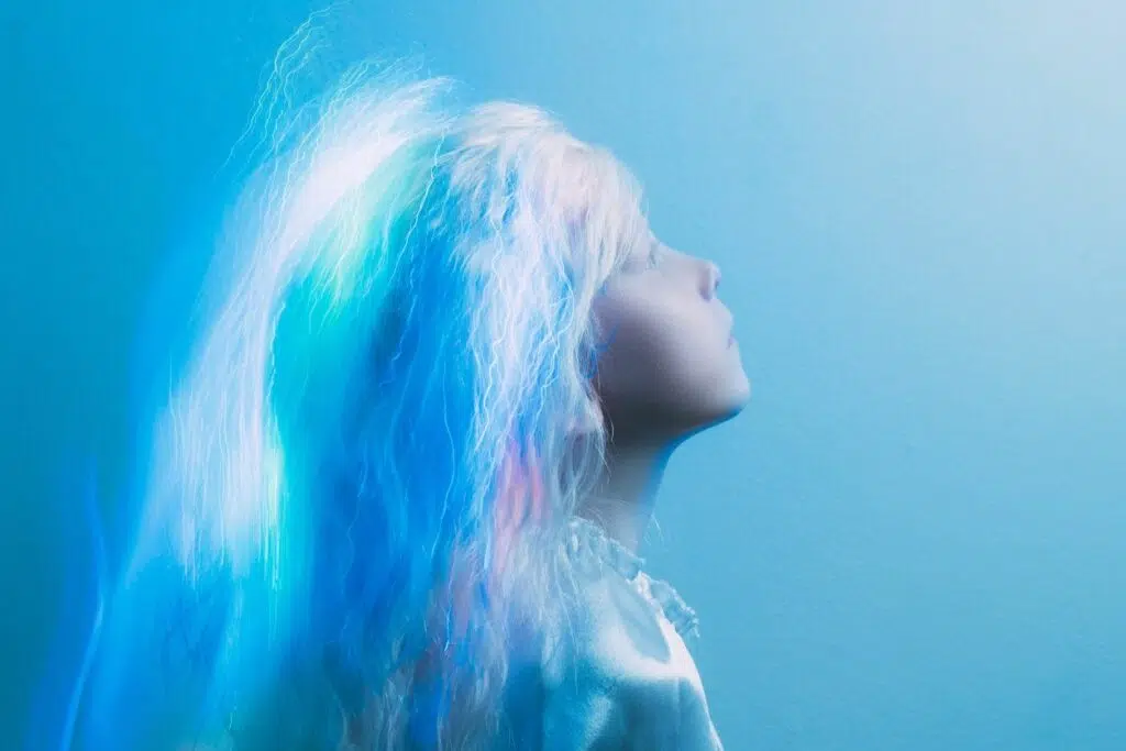 jeune fille aux cheveux très clairs presque blancs et bleus vue de profil regardant vers le haut sur un arrière plan bleu