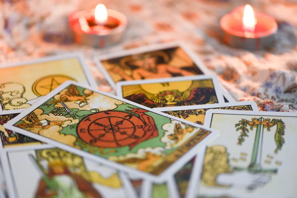 des cartes de tarot éparpillées sur une table avec des bougies en fond. 